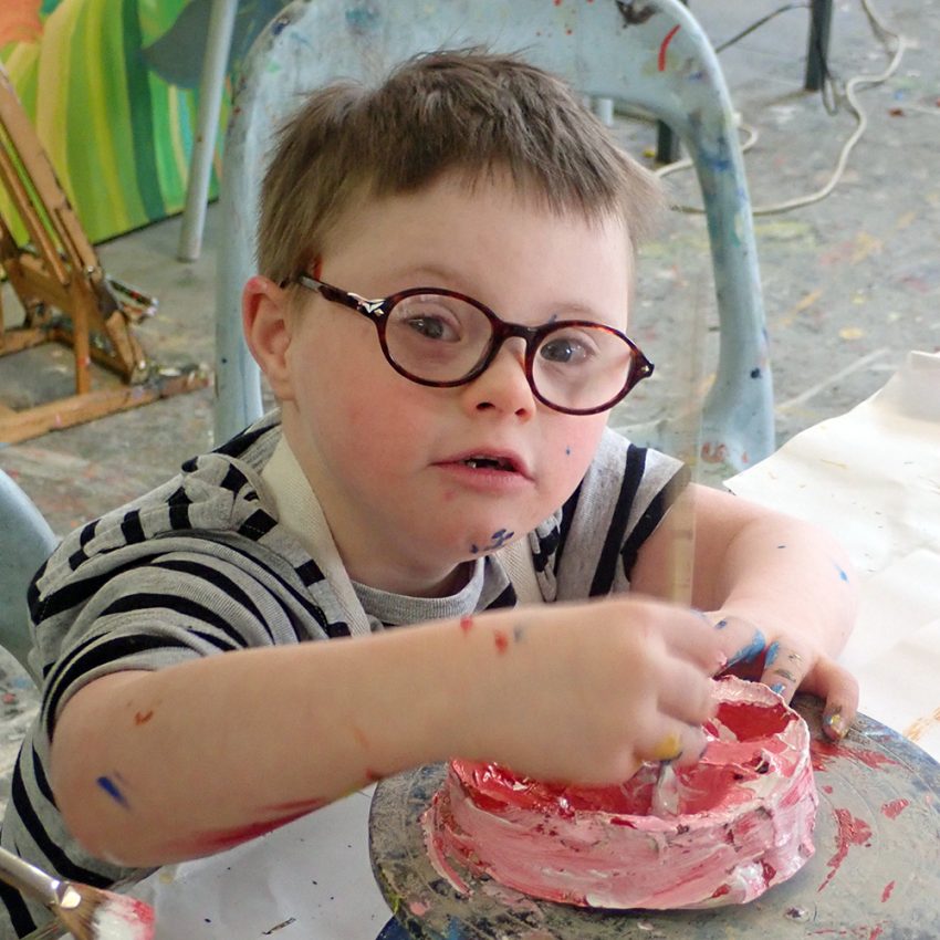 Young boy using red and white paint to paint a clay mould