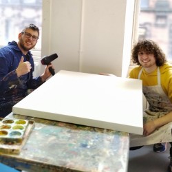 two men sitting either side of a large canvas in the studio