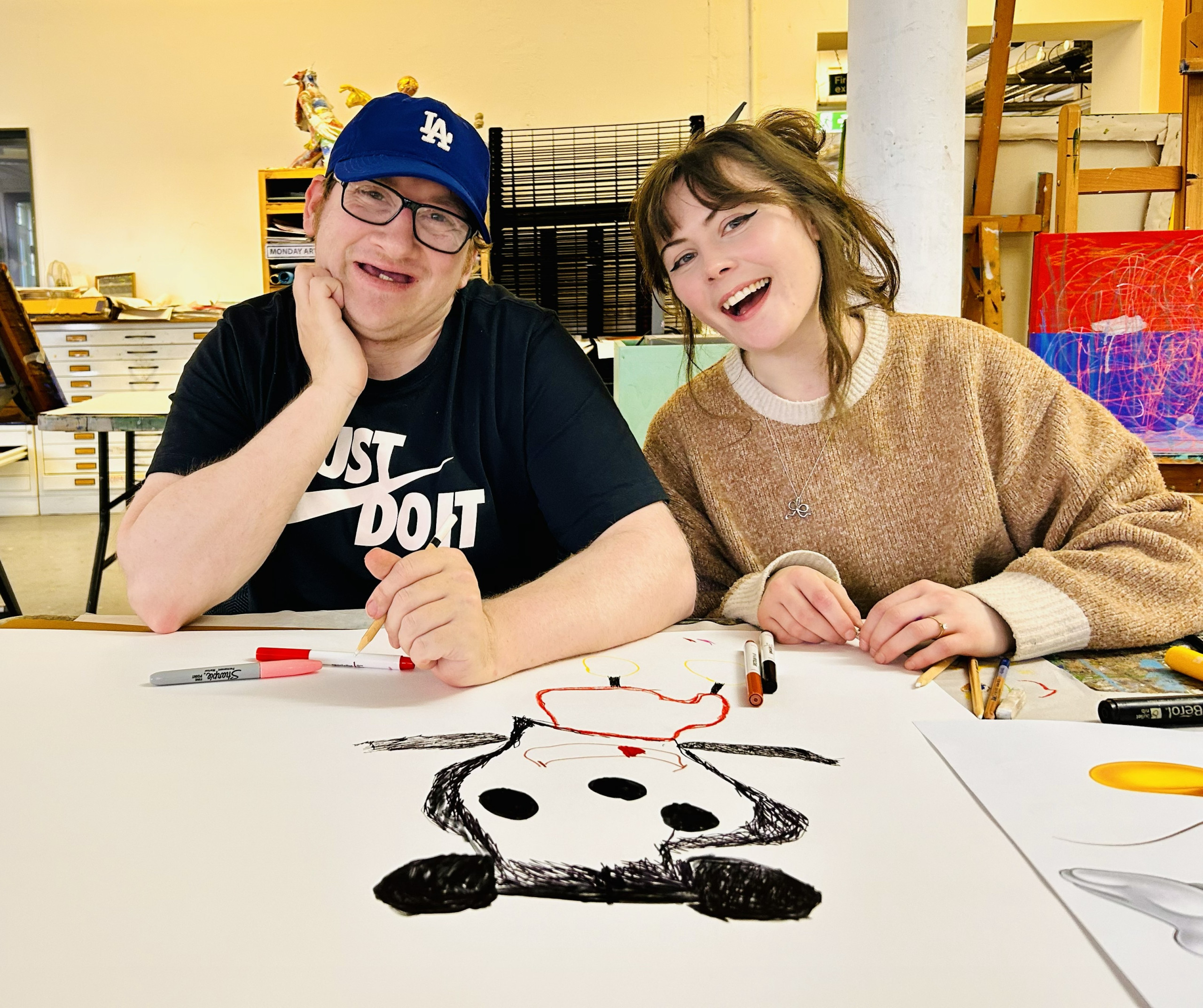 a volunteer sitting beside an artist at a desk in the studio