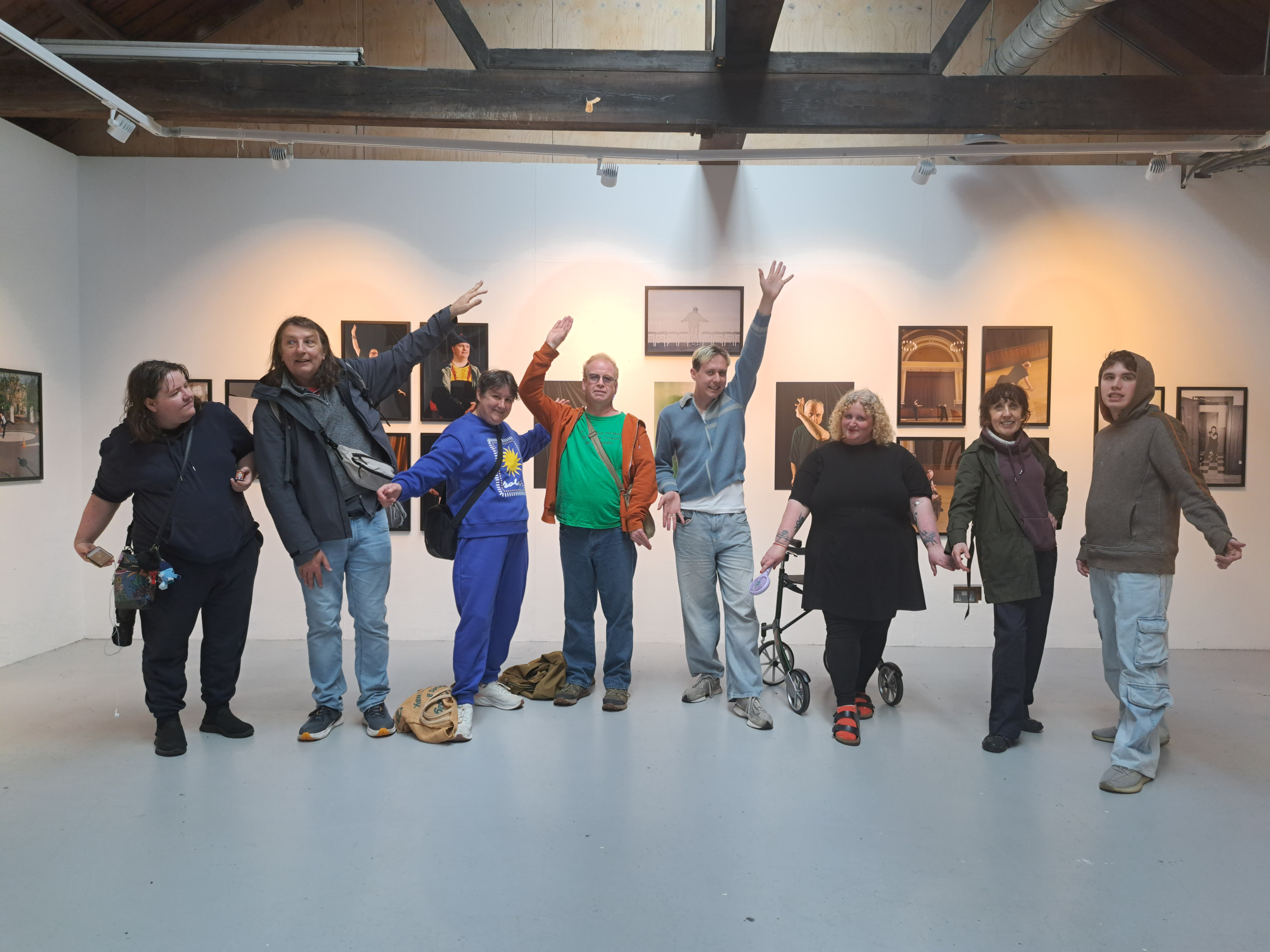 Diverse group of nine people pose in an art gallery, smiling and raising arms