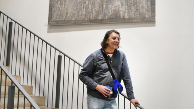 An artist poses on the stairs underneath a painting at the exhibition opening event