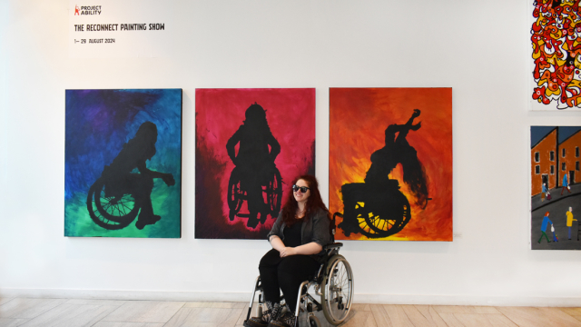The artist poses smiling in front of her tryptic of paintings.