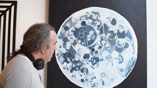 A viewer looks at a painting of the moon on the wall at the exhibition opening event