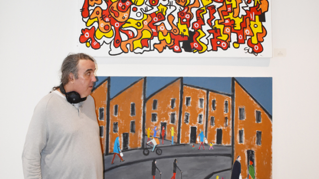 An artist stands in front of two paintings at the exhibition opening event