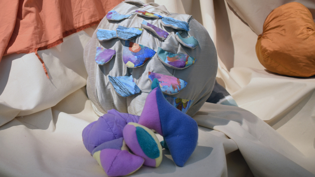 A photography showing a close up image of one of the fabric shapes. This is a large silver spherical piece covered with semi circular scales in a bright multicoloured print.