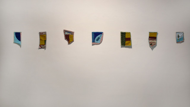 An exhibition photograph showing a row of small quilted pieces on the wall.