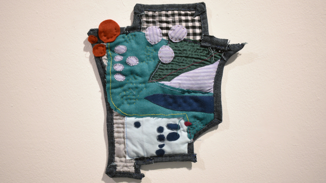 A close up of a small quilted piece. An irregular shape made up of collaged fabrics, with visible stitching and appliqued circles in different colours.