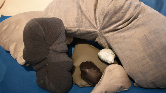 A close up photograph of the installation showing smaller stuffed fabric objects nestling under a larger v shaped silver shape.