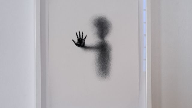 A shadowy painting of a person's shape with a hand out, in black ink.