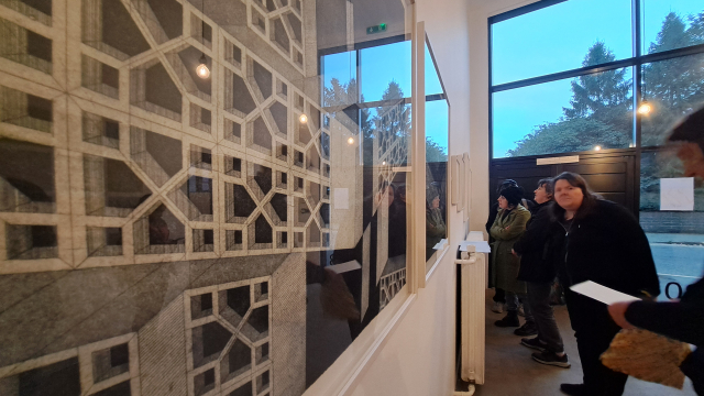Large black and white geometrical prints inside glass frames on a gallery wall. There are people looking at the art.