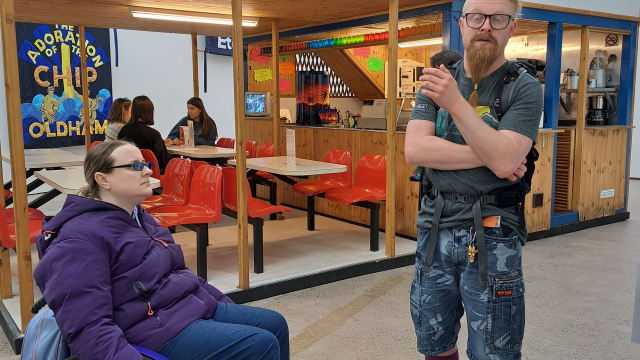 A wheelchair user and someone else gather outside of a pop up café inside of a gallery.