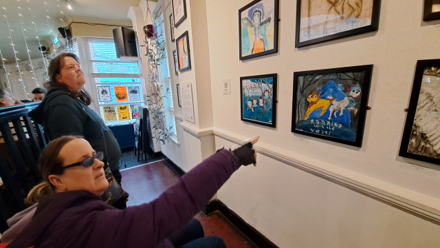 Two people are in a café space that has several vinyl sized artworks on the wall.