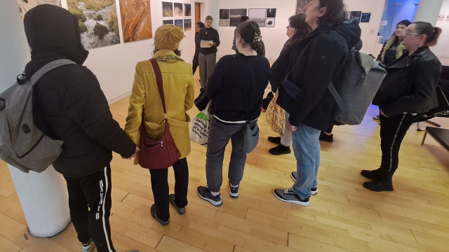 A close up of a group of people in a gallery space, their backs to the camera as they look at the art.