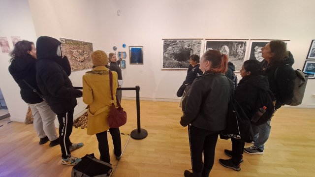 A group of people gather at a spacious gallery space, looking at the artworks.