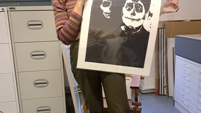 A person holds up a black and white print of two people who have skull face paint on.