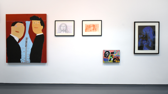 A photograph of the exhibition showing portraits of musicians in a variety of styles. There are drawings and prints as well as paintings using strong blocks of colour and one using electric blue pencils on a black background to depict a singer.