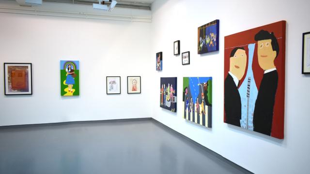 A photograph of the exhibition showing paintings of different sizes and subjects including the beatles on a zebra crossing and dorothy on the yellow brick road.