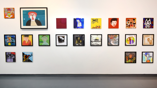 A photograph of the exhibition showing rows of paintings inspired by record covers and one larger portrait of Elton John painted in teal, red and white colours.