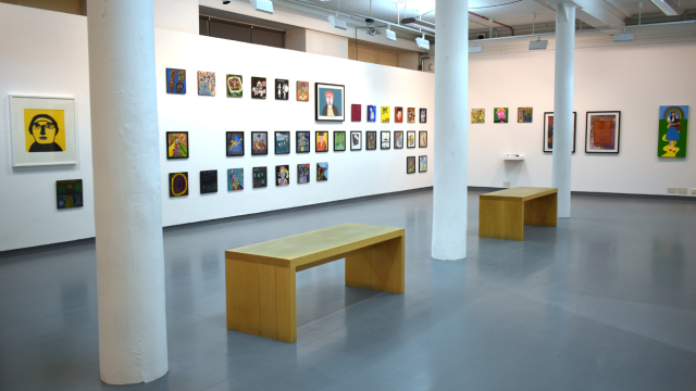A photograph of the exhibition showing rows of paintings inspired by record covers and some larger paintings of bands, portraits of musicians and music inspired artworks. There are benches in the centre of the space.