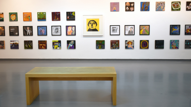 A photograph of the exhibition showing rows of paintings inspired by record covers and one larger portrait of Phil Collins in bold black pen on a yellow background.