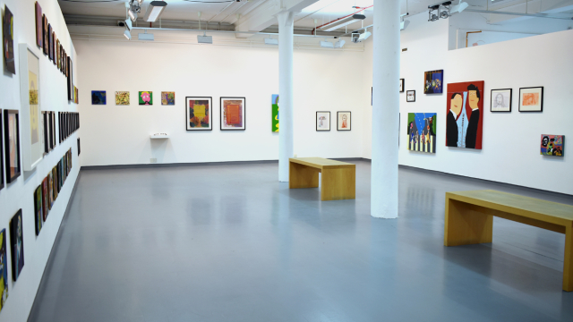 A photograph of the exhibition showing rows of paintings inspired by record covers and some larger paintings of bands, portraits of musicians and music inspired artworks. There are benches in the centre of the space.