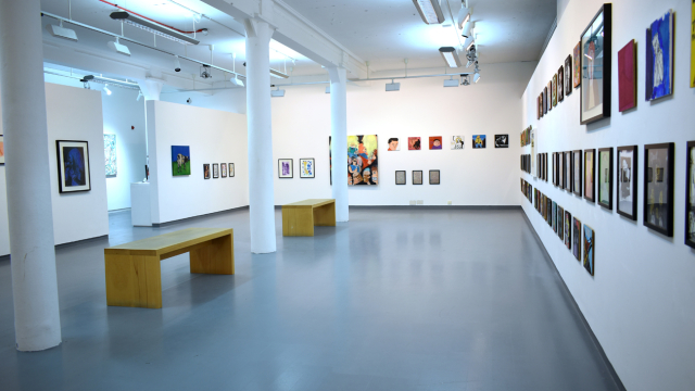A photograph of the exhibition showing rows of paintings inspired by record covers and some larger paintings of bands and portraits of musicians. There are benches in the centre of the space.