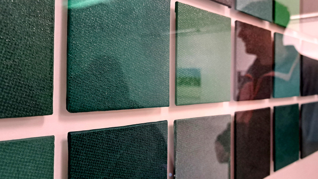 The shadow of a man reflects on green glassy tiles on a wall.