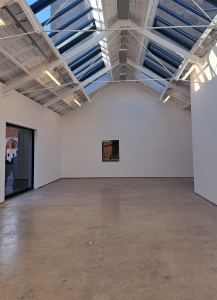an open view of part of the gallery. There is no one in the gallery. You can see one painting on the far wall and a large glass window to the left