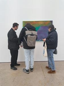 Three people stand in front of a painting / mixed media artwork which hangs on a white gallery wall.