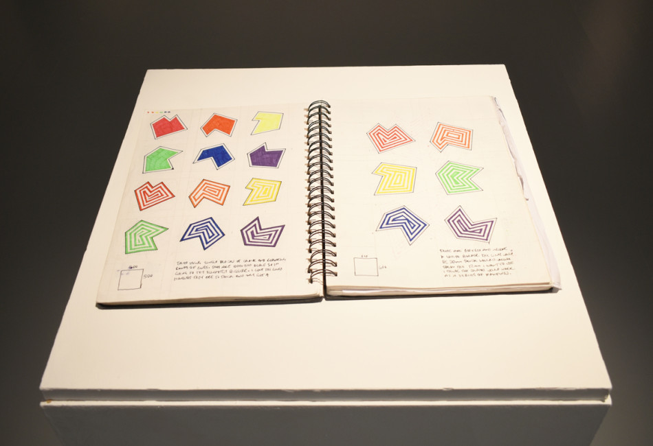 A photograph of an open sketchbook. Inside are abstract colourful geometric shapes.