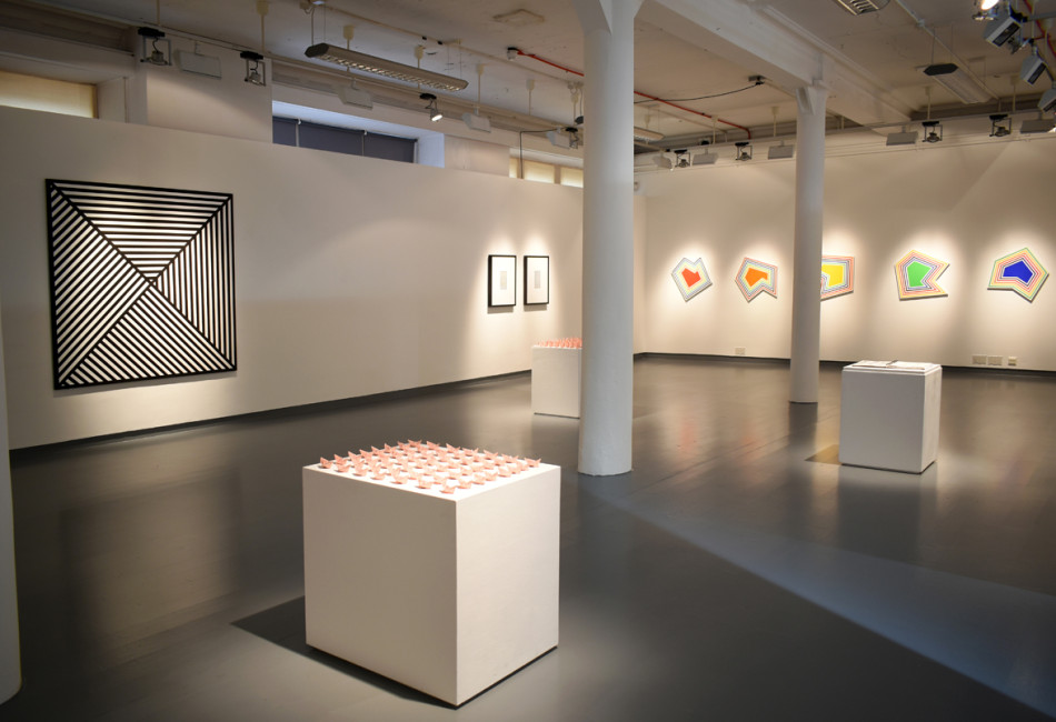 Photograph of the exhibition view showing plinths with origami work, abstracted shape paintings and geometric work.