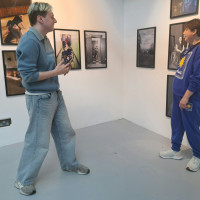 A photographer waits to photograph a woman in a modern gallery, surrounded by photographs