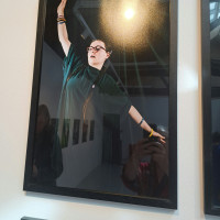 Framed portrait of a smiling performer with arms outstretched, wearing glasses and dark clothing.